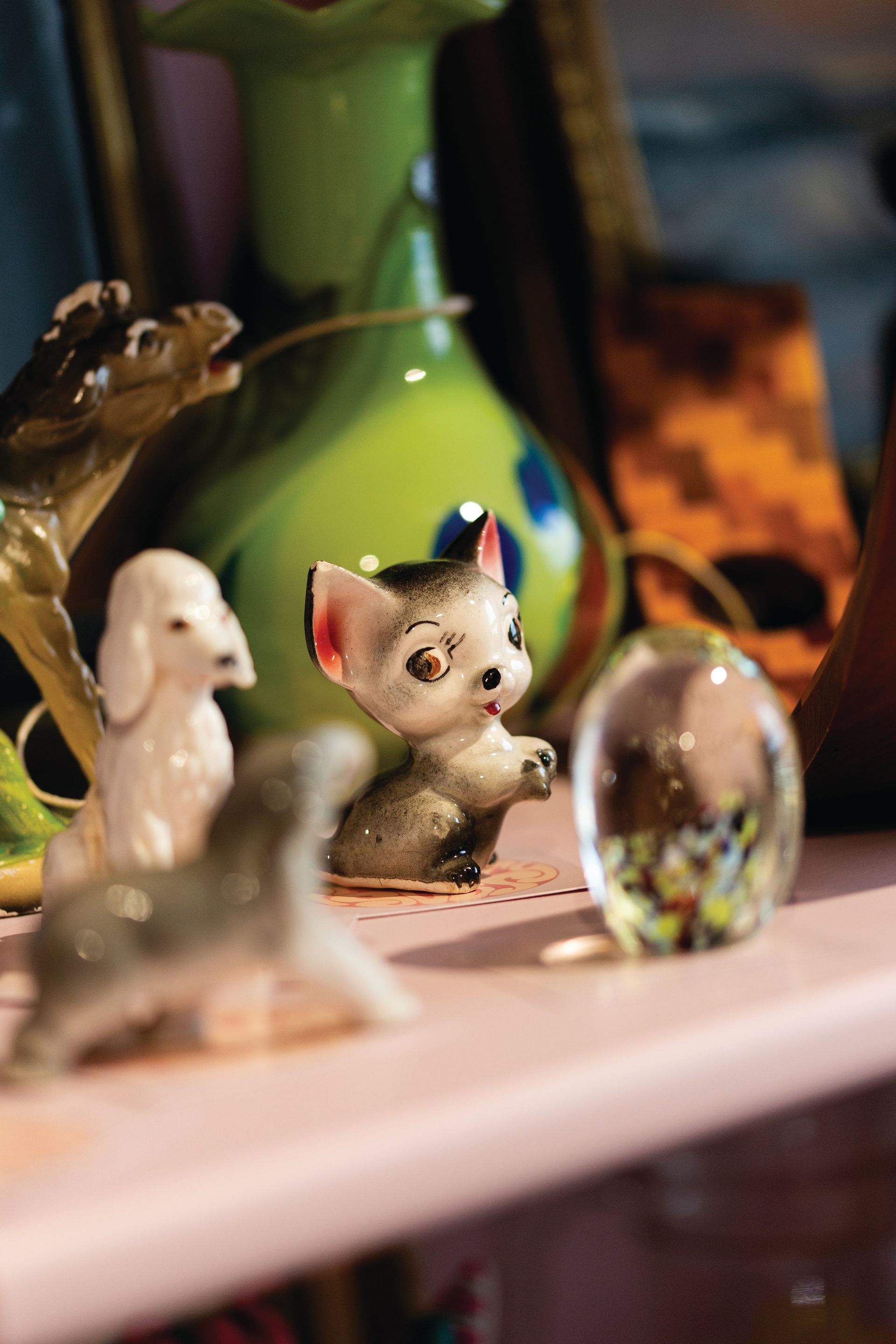 A shelf displaying ceramic animal figurines, a glass paperweight, and a green vase.
