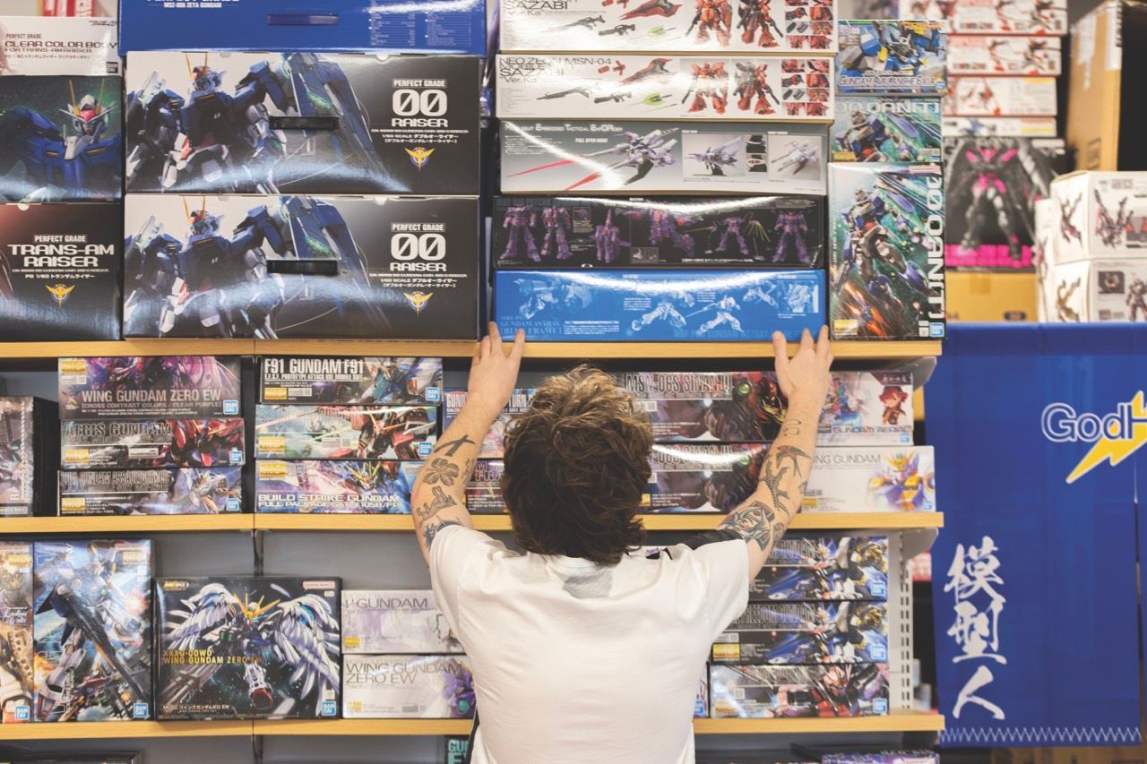 Person reaching for a model kit on a shelf filled with model kits in a store. Arm tattoos visible.