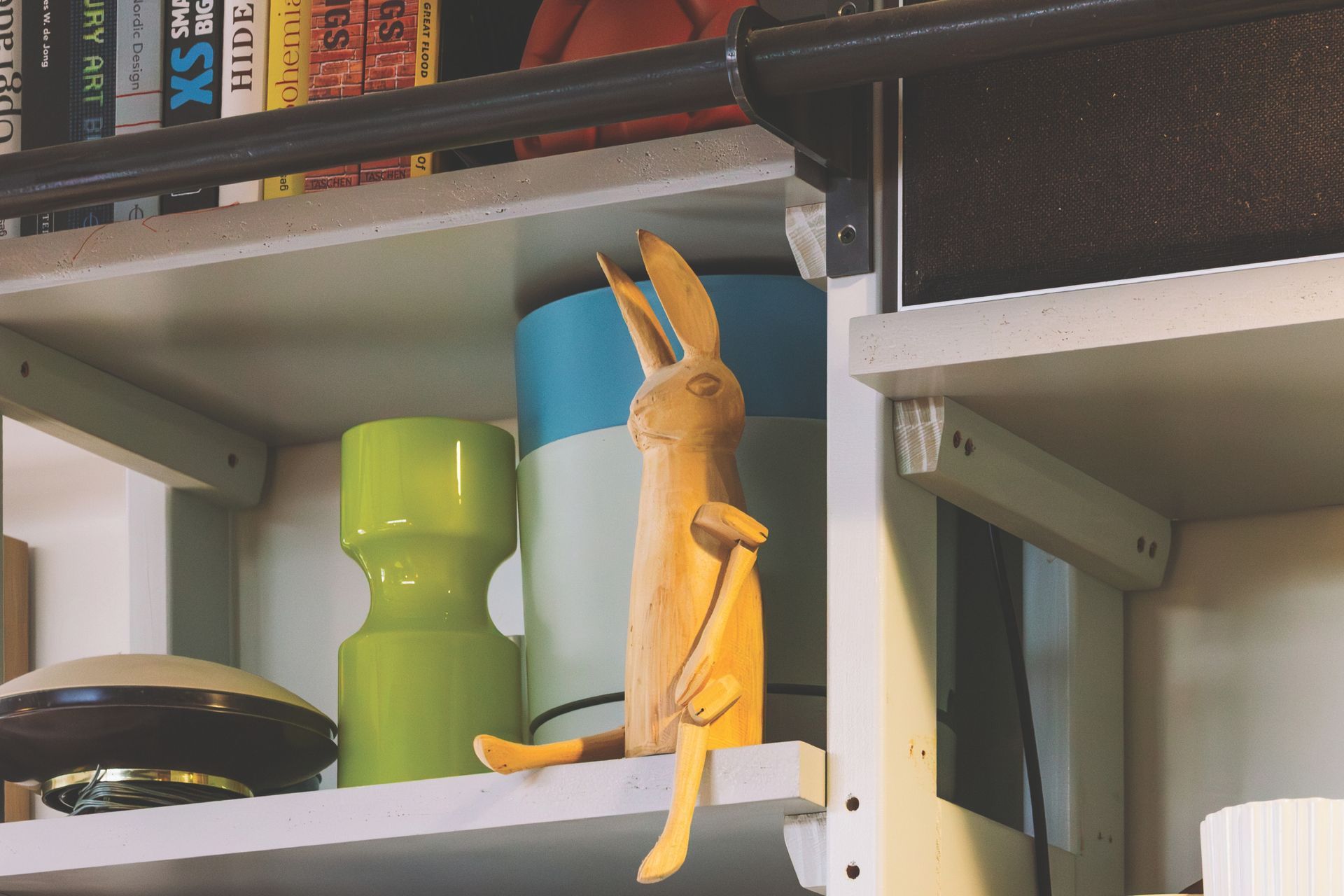 Wooden rabbit figurine perched on a white shelf with various objects, including vases and books.