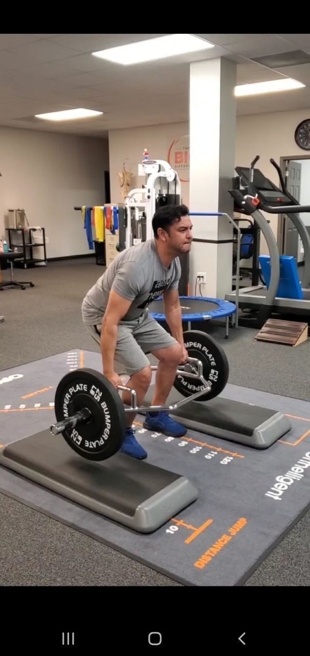 a man is lifting a barbell in a gym - using strength training to benefit his physical therapy 