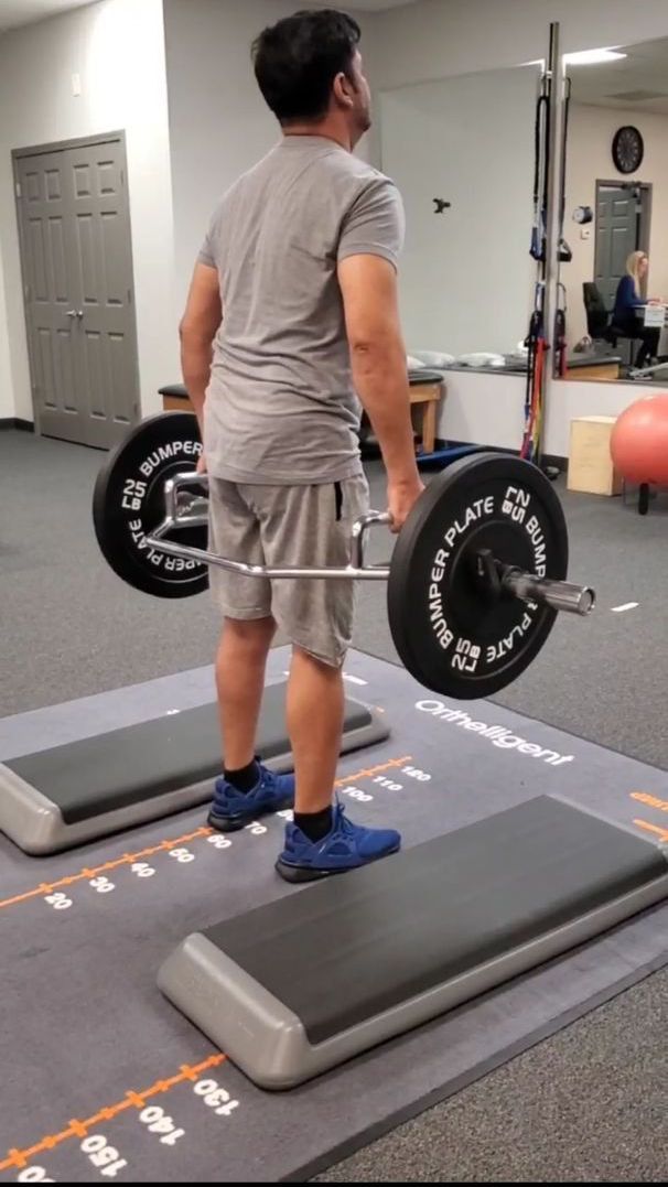 a man is lifting a hex bar with weight plates for strength training