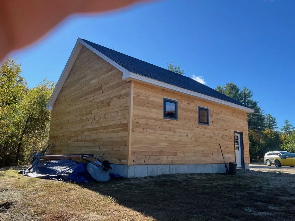 A wooden house with a black roof is sitting in the middle of a field.
