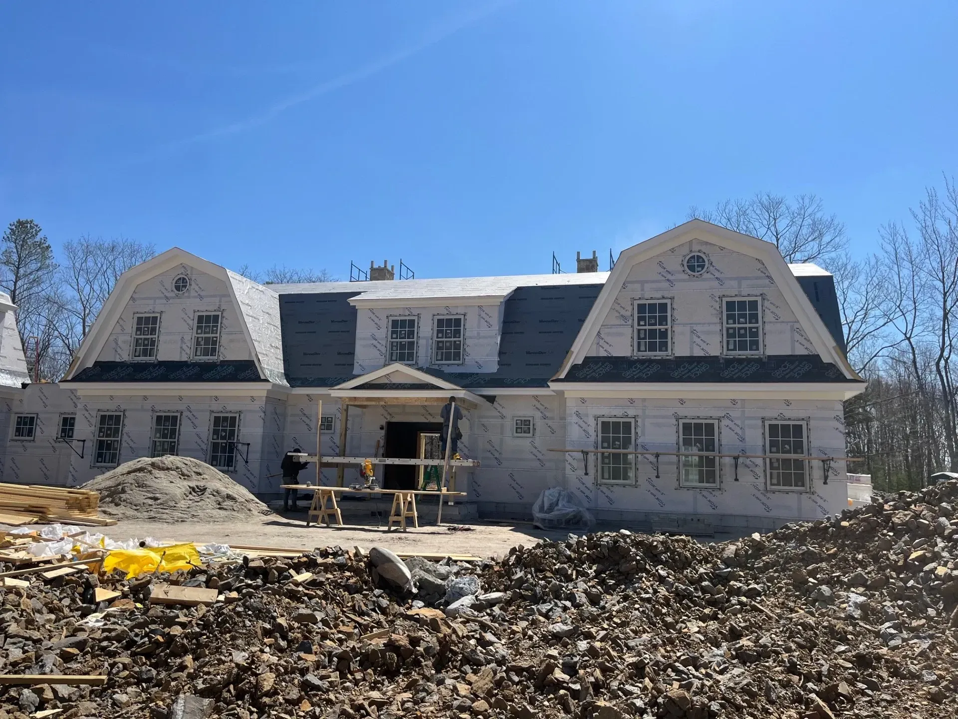 A large white house is being built in the middle of a dirt field.
