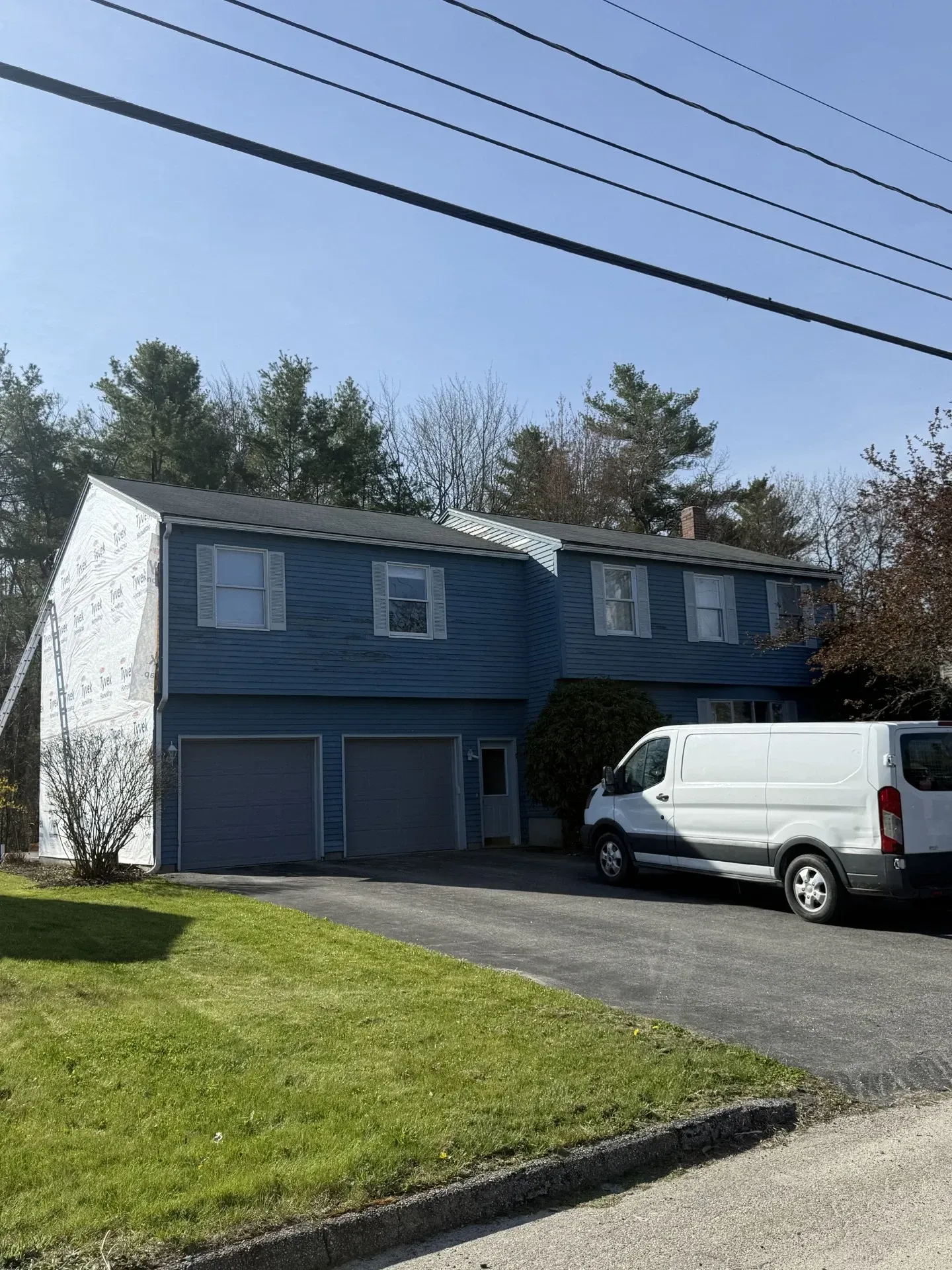 Blue two-story house with garage, white van parked in the driveway, and a grassy front lawn under clear skies