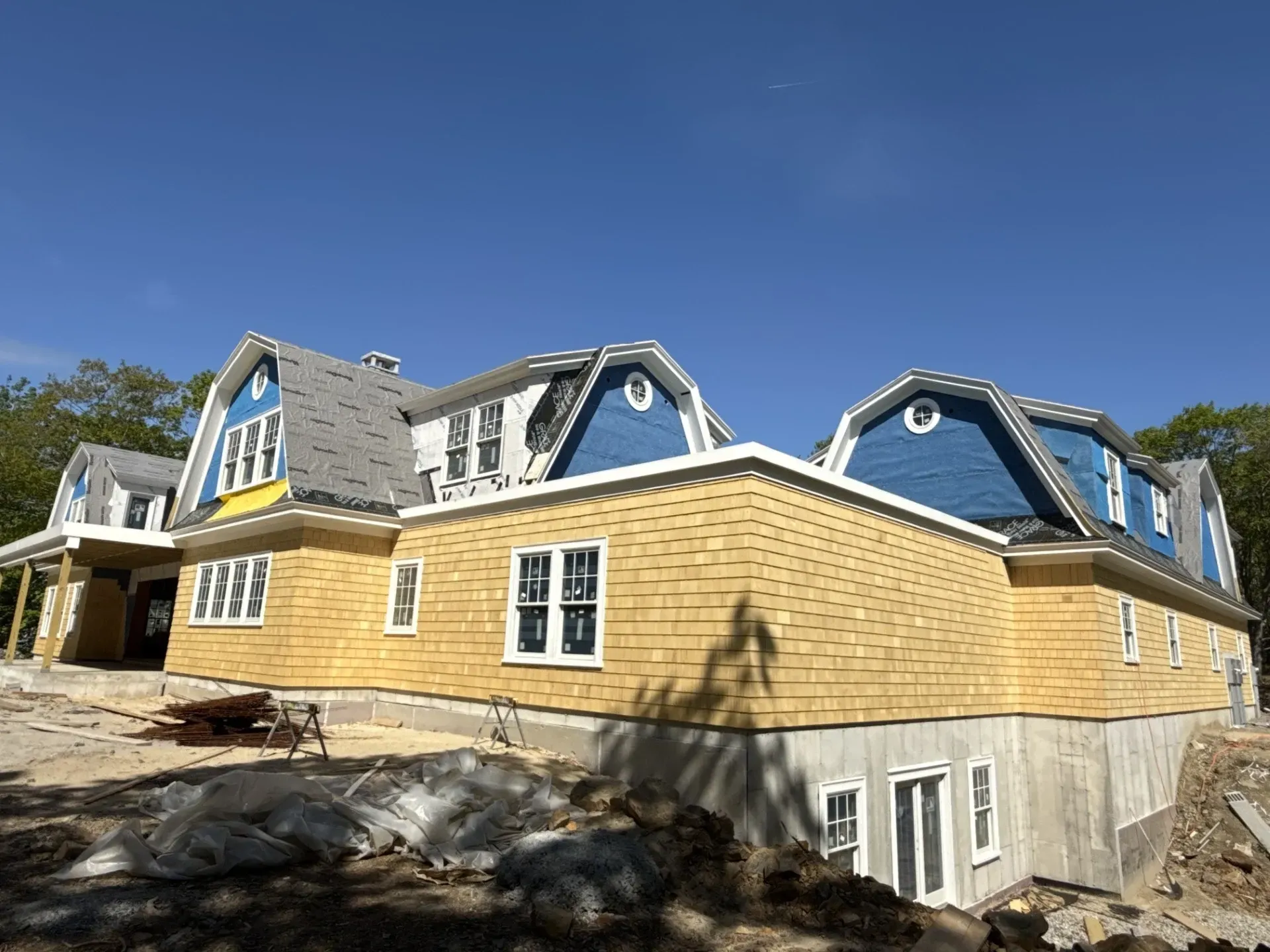 A large house is being built with yellow siding and blue roofs.