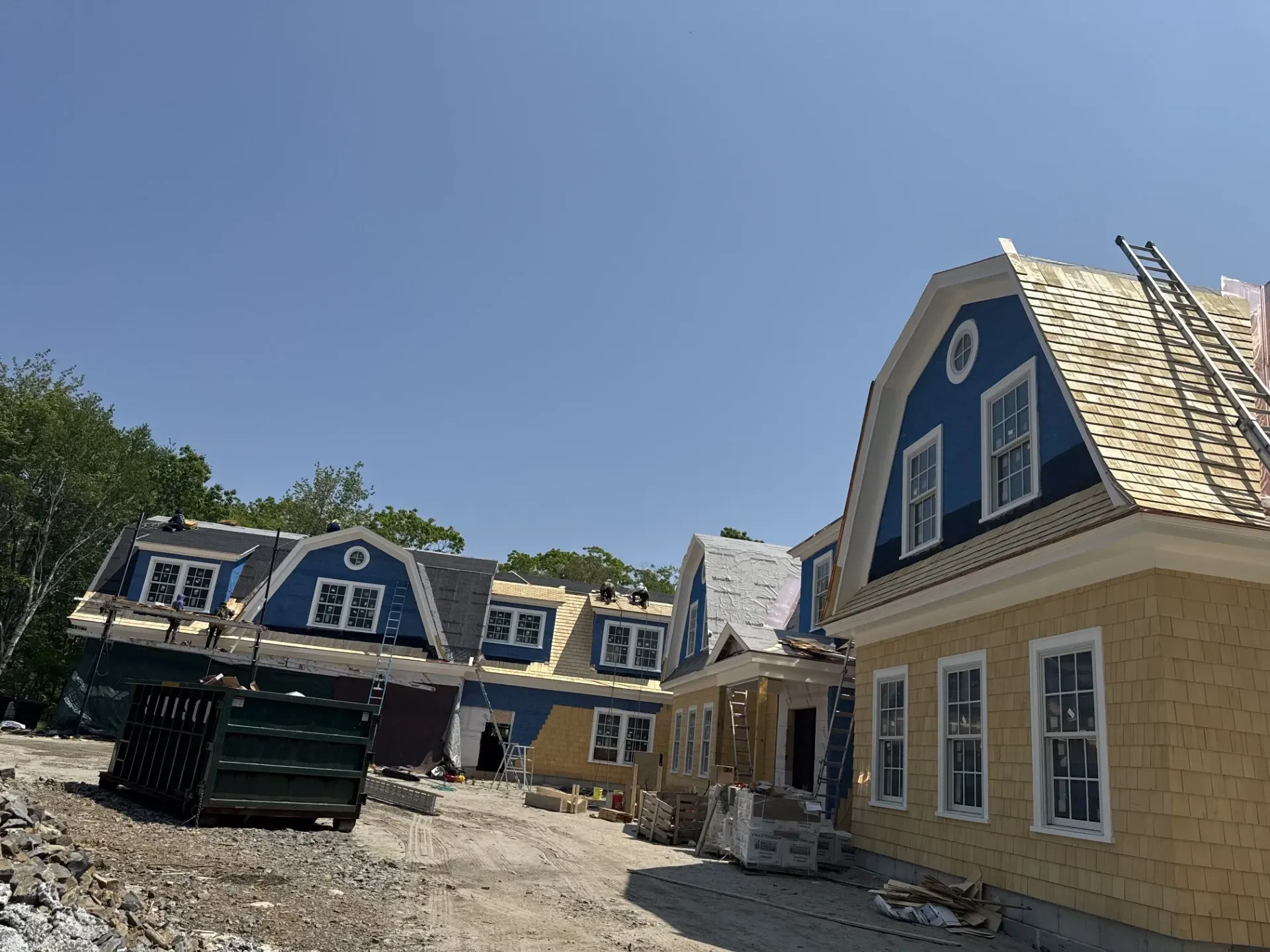 A row of houses under construction with a dumpster in the foreground.