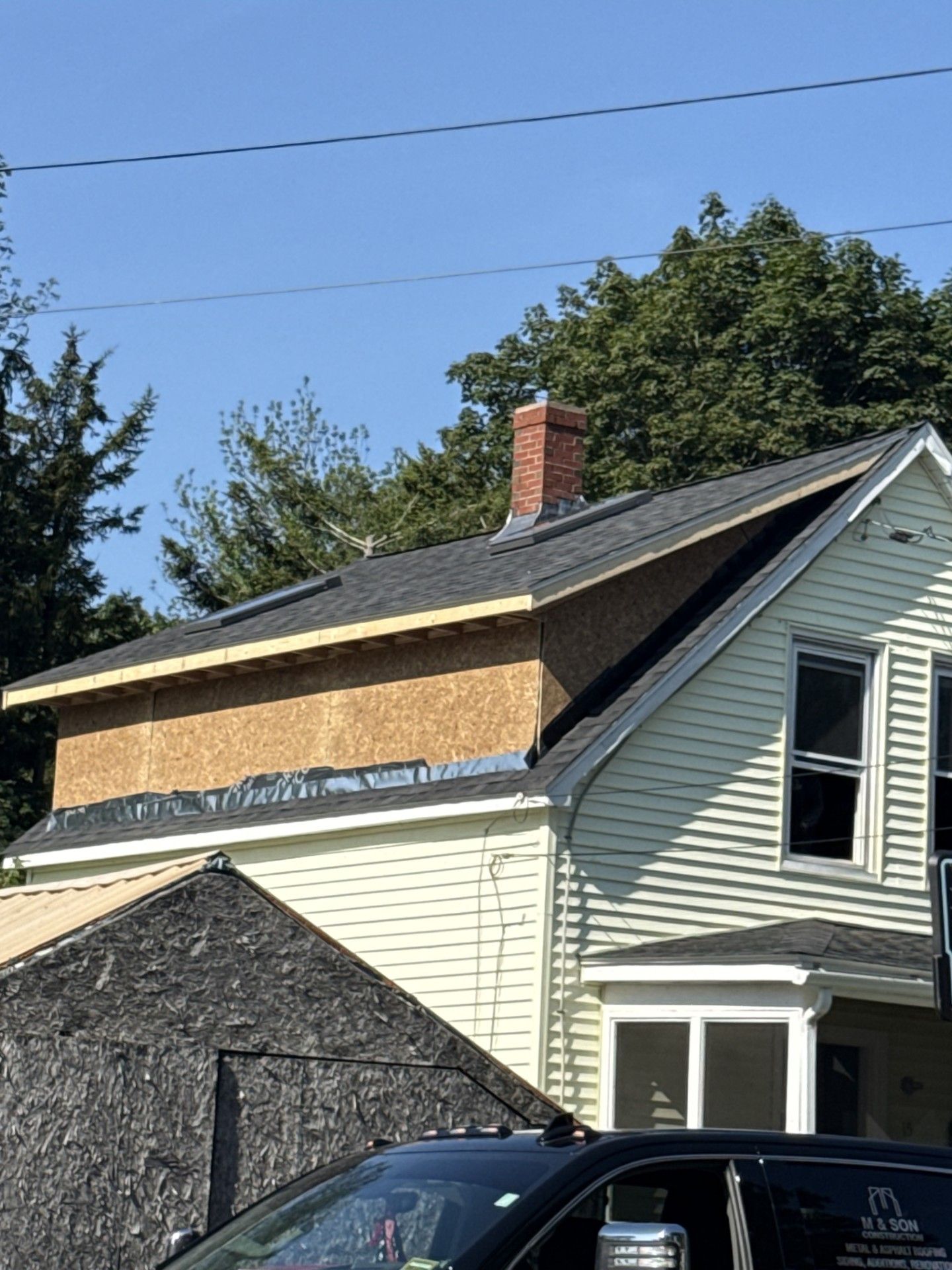 House undergoing roof repair; new sheathing visible, brick chimney on top.