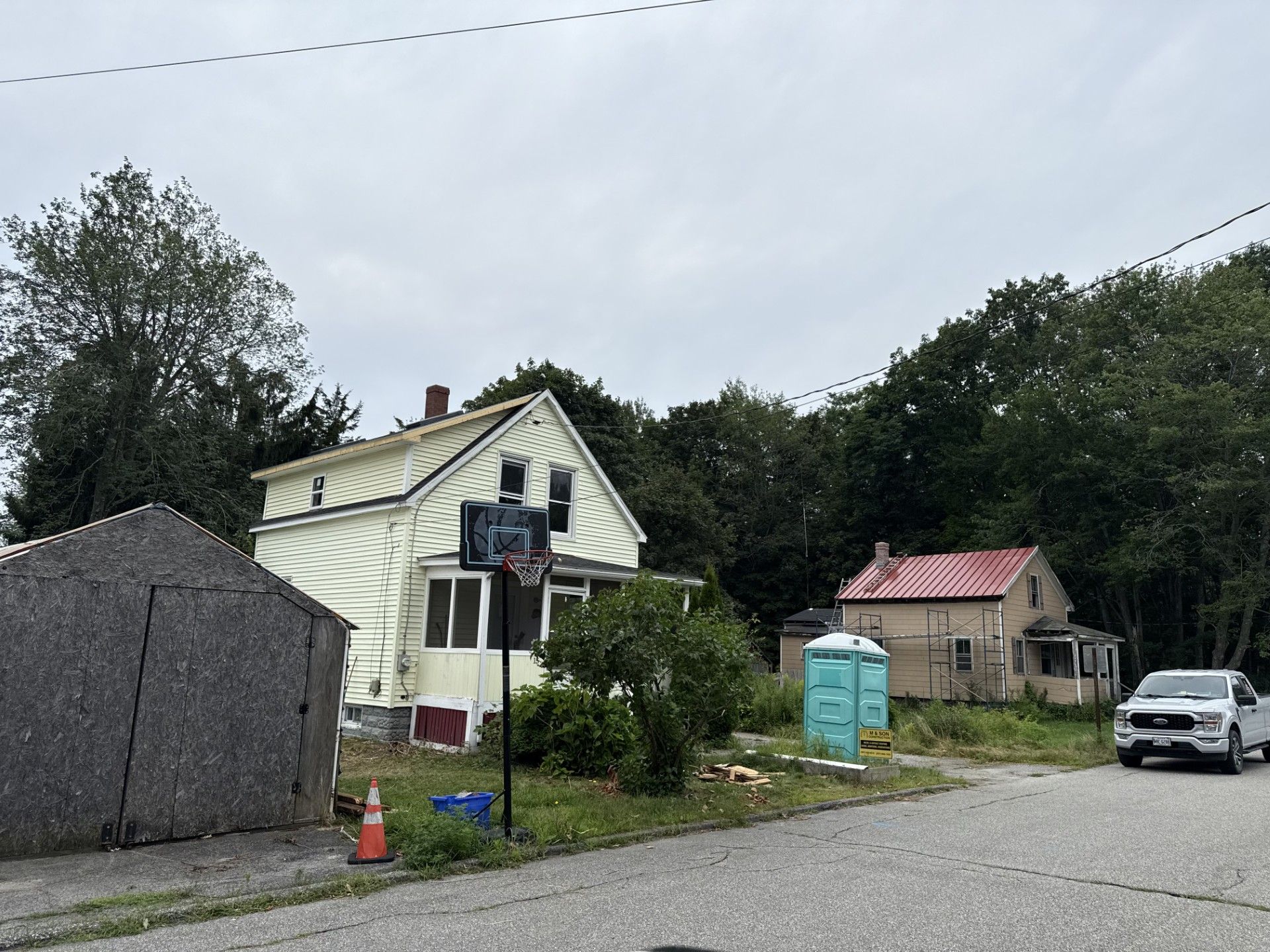 Houses under renovation, cloudy day, portable toilets, white truck parked on road.