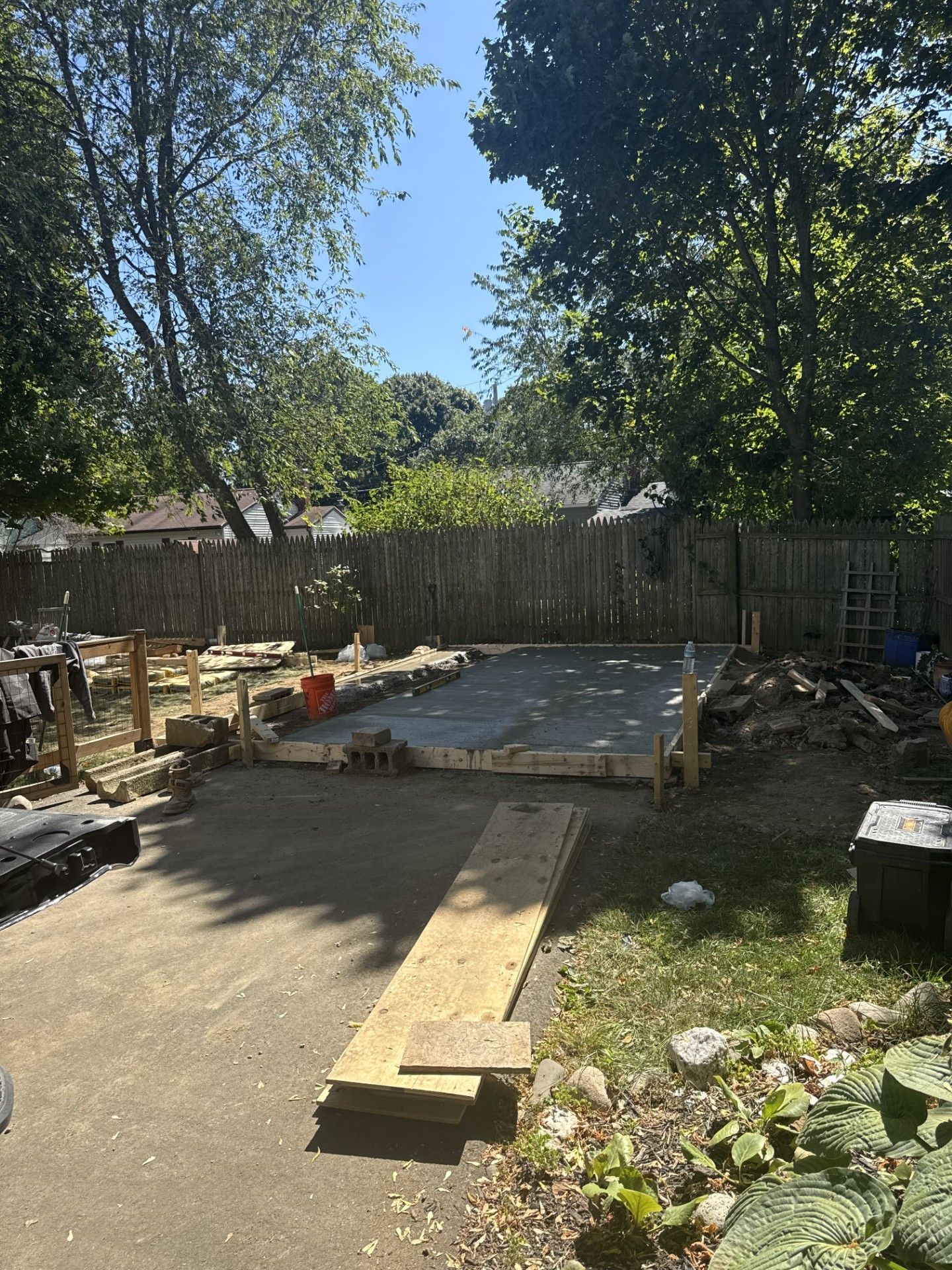 Backyard construction site; concrete slab with wooden frame, lumber, and tools.