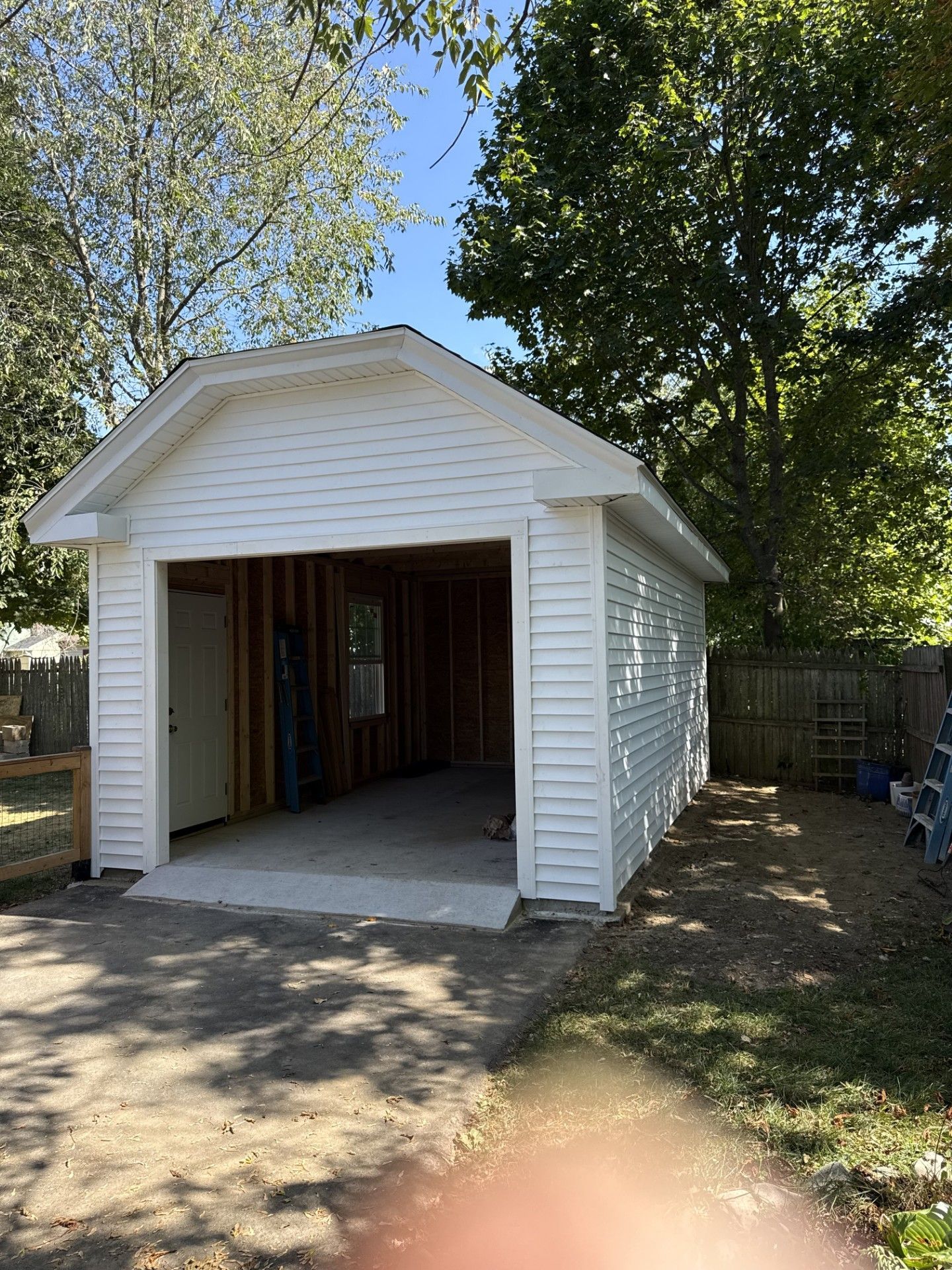 White-sided detached garage with open doorway, concrete floor, and wooden framing visible inside.