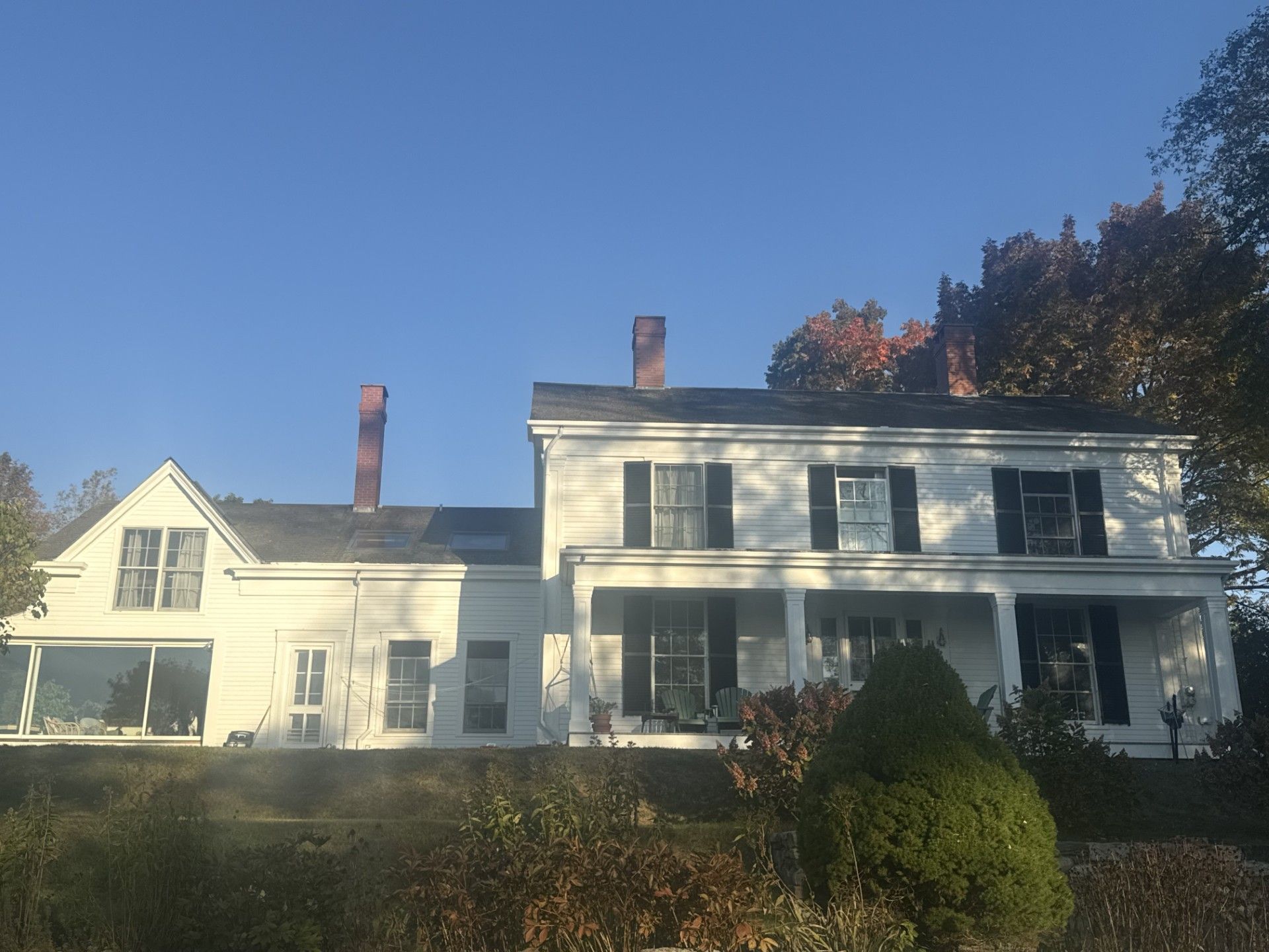 White two-story house with black shutters, a porch, and red brick chimneys against a clear blue sky.
