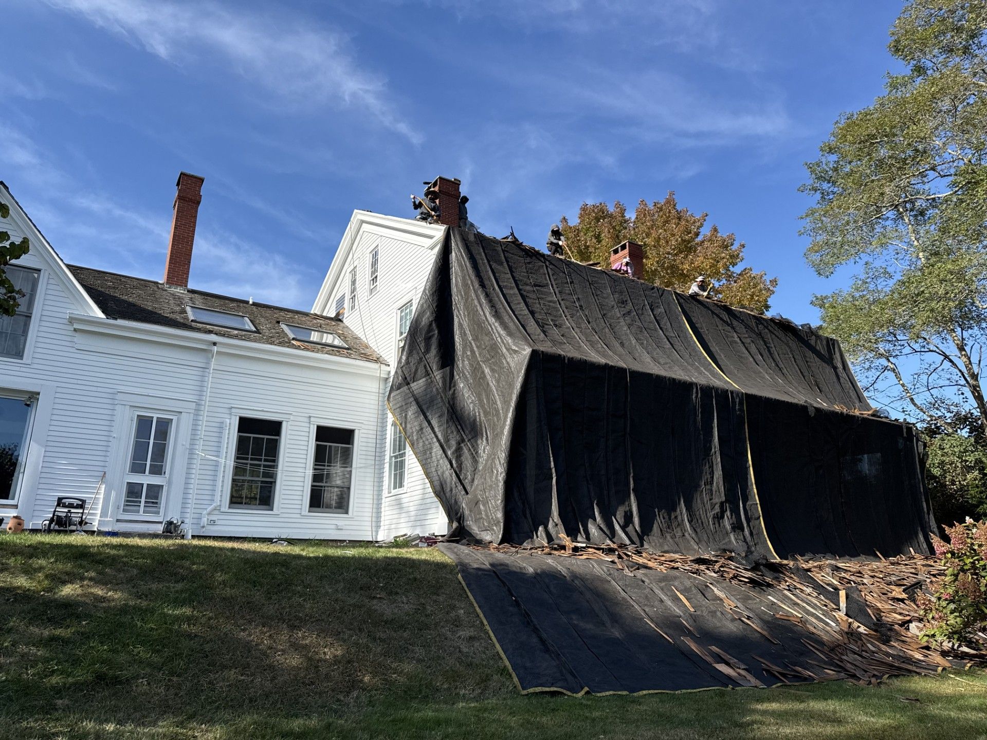 White house with a damaged roof covered by black tarp.