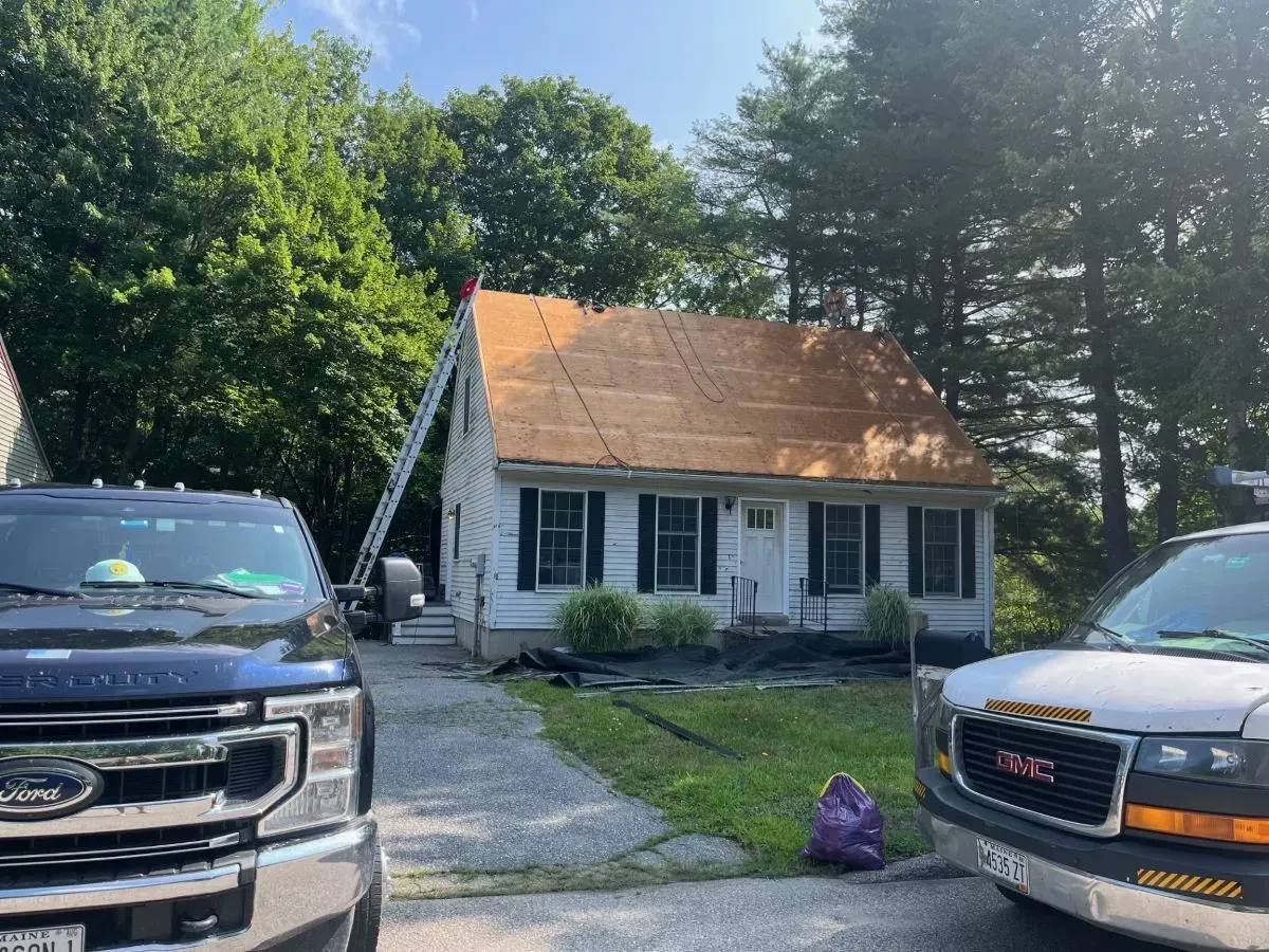 Two trucks are parked in front of a house with a ladder on the roof.