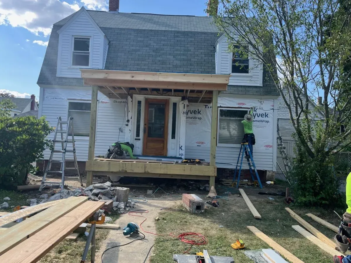 A white house is being remodeled with a wooden porch.