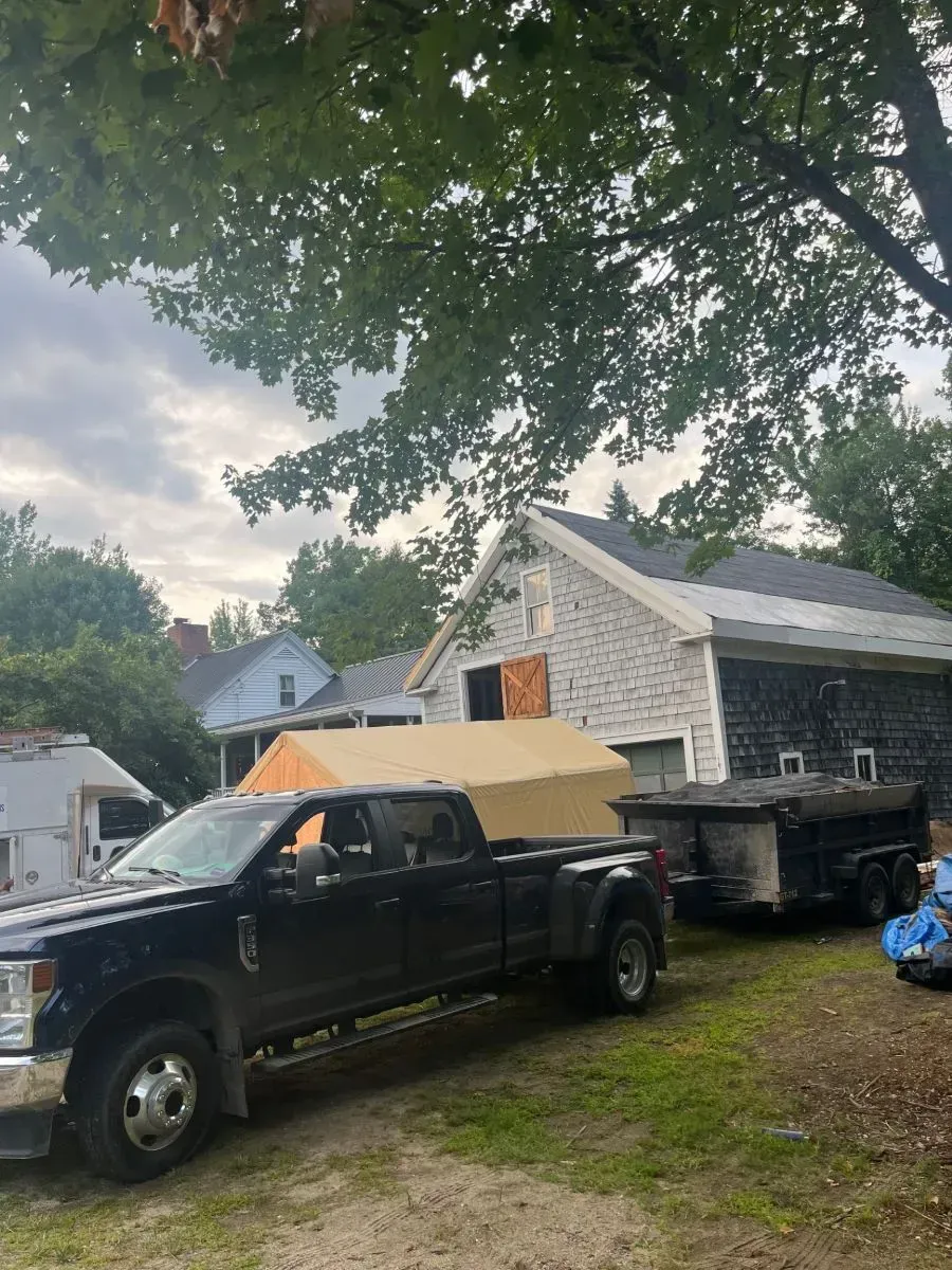 A black truck is parked in front of a house with a trailer attached to it.