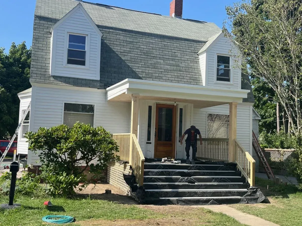 A man is standing on the porch of a white house.