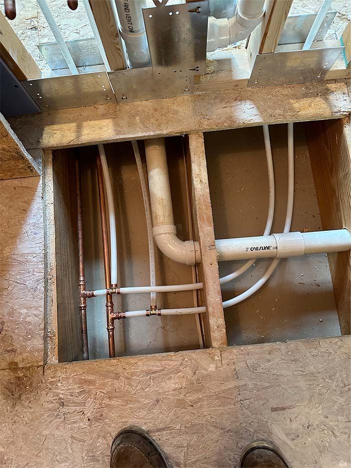 A person is standing in a hole in the floor with pipes coming out of it.