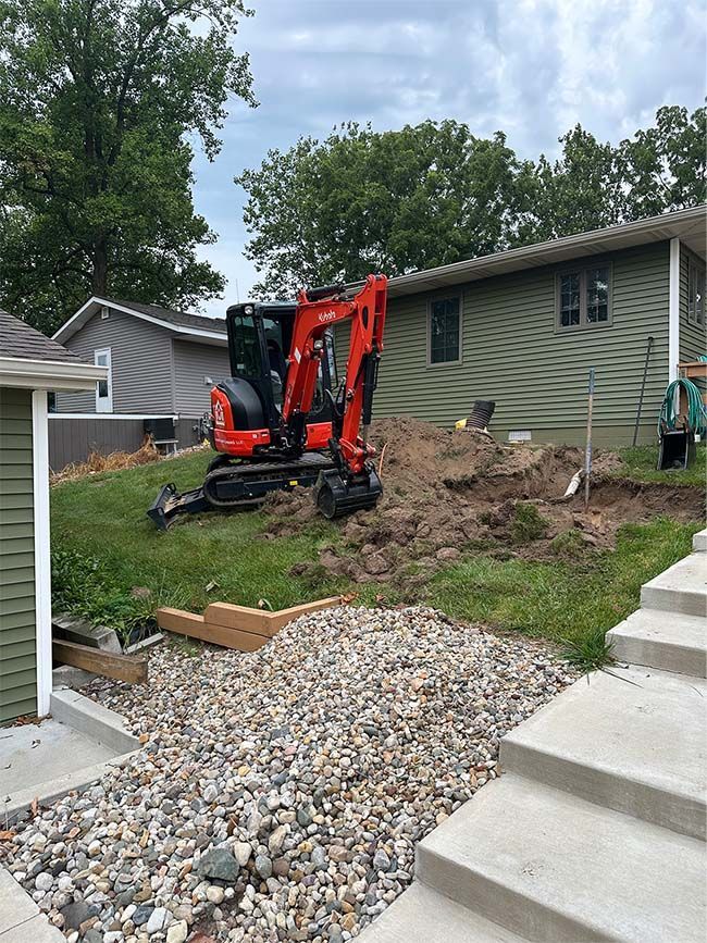 A red and black excavator is sitting in front of a house.