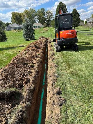 A small excavator is digging a trench in a yard.