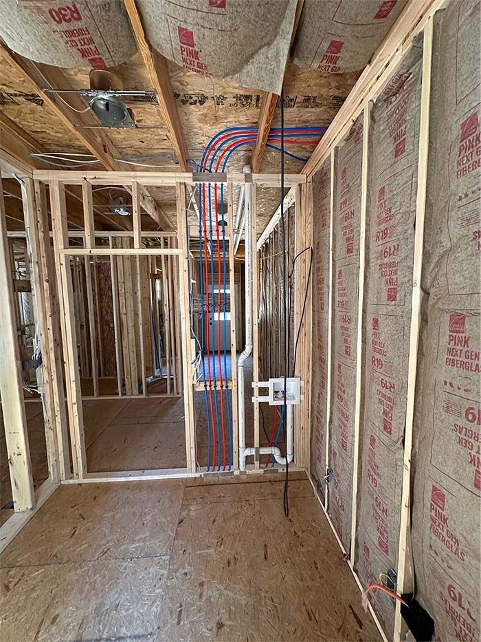 A room in a house under construction with a lot of pipes coming out of the ceiling.
