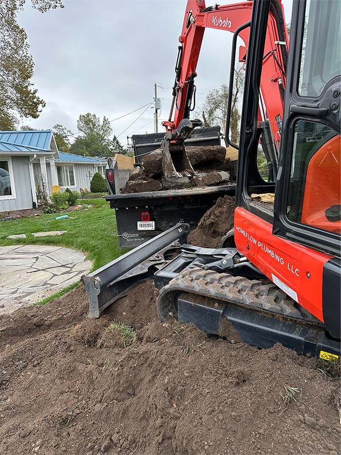 A red excavator is digging a hole in the ground in front of a house.