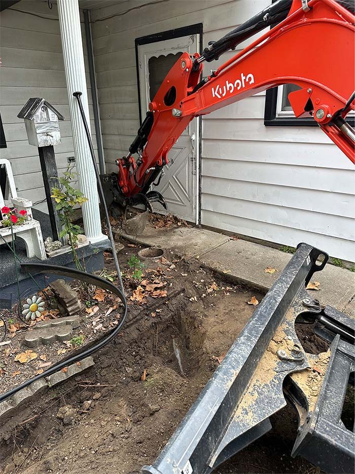 A red excavator is digging a hole in the ground in front of a house.