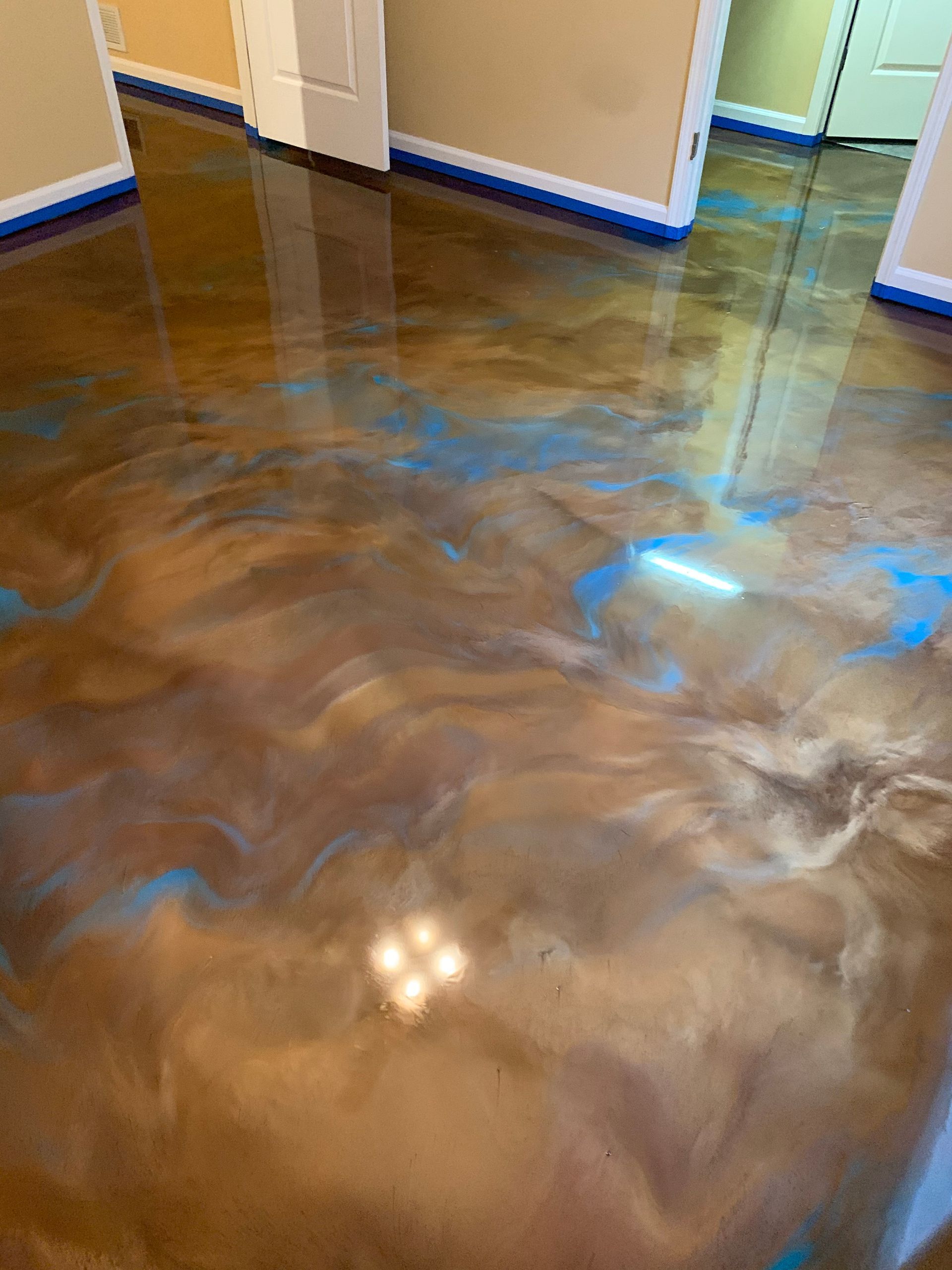 A glossy, metallic epoxy floor featuring swirling shades of brown, bronze, and bright blue, reflecting interior lighting.
