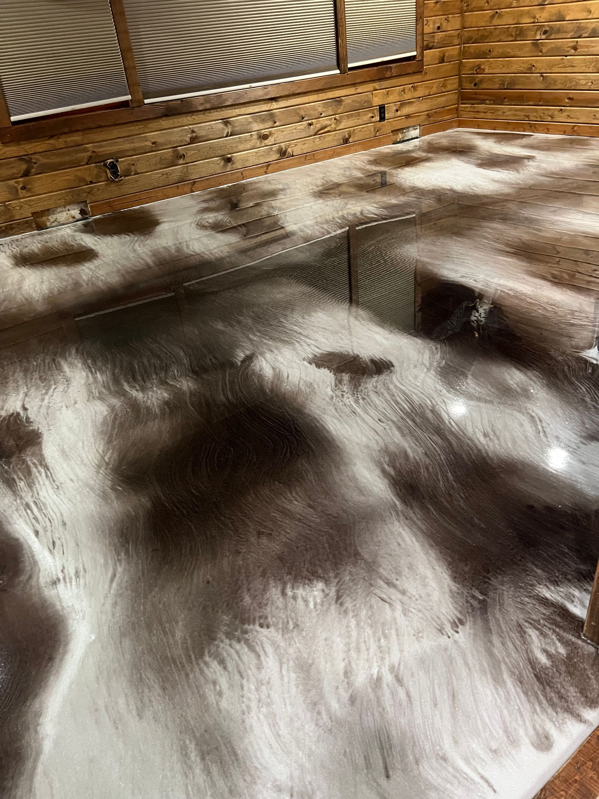 A high-gloss epoxy floor featuring a swirling, marbled pattern of dark brown and white, set against wood-paneled walls.