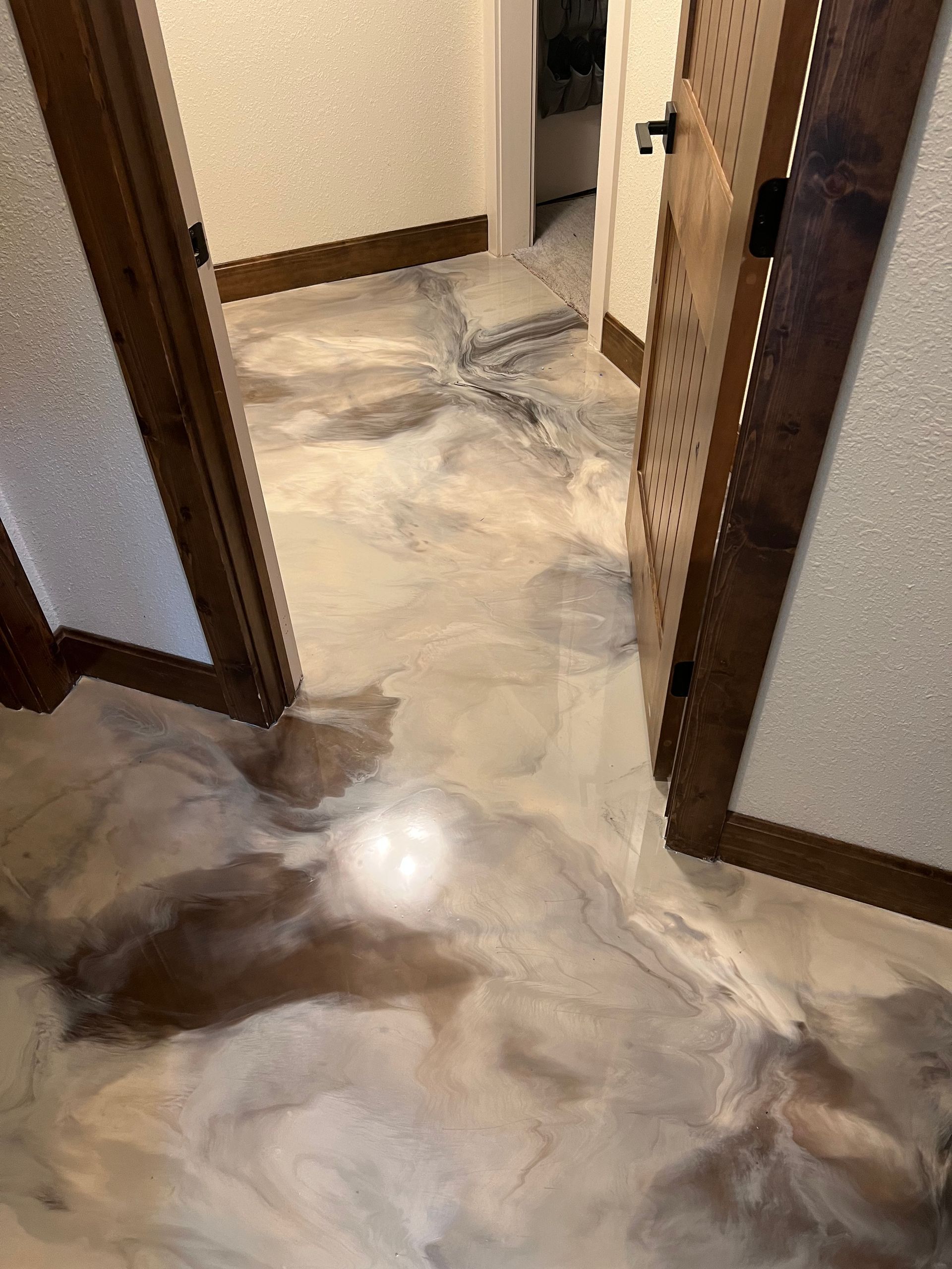 A hallway with a beige and grey marbled epoxy floor, showing a star-shaped pattern in the distance near a wooden doorway.