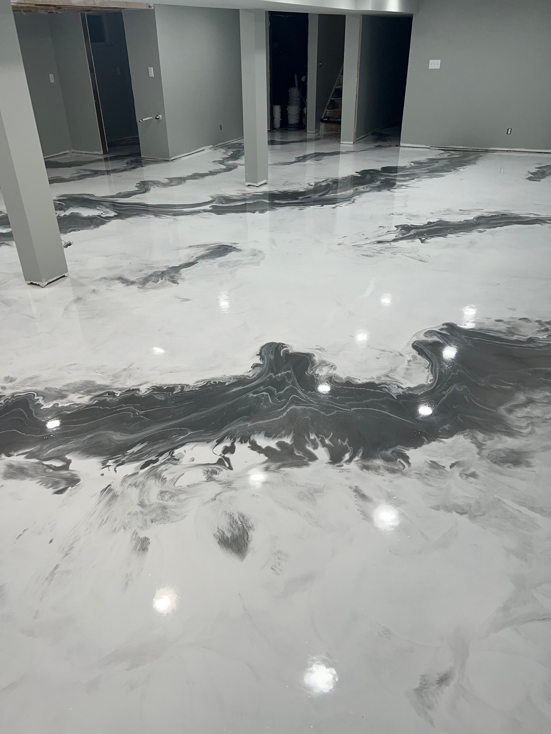 A glossy, white epoxy floor with marbled, dark gray swirled accents in a room with several structural support columns.