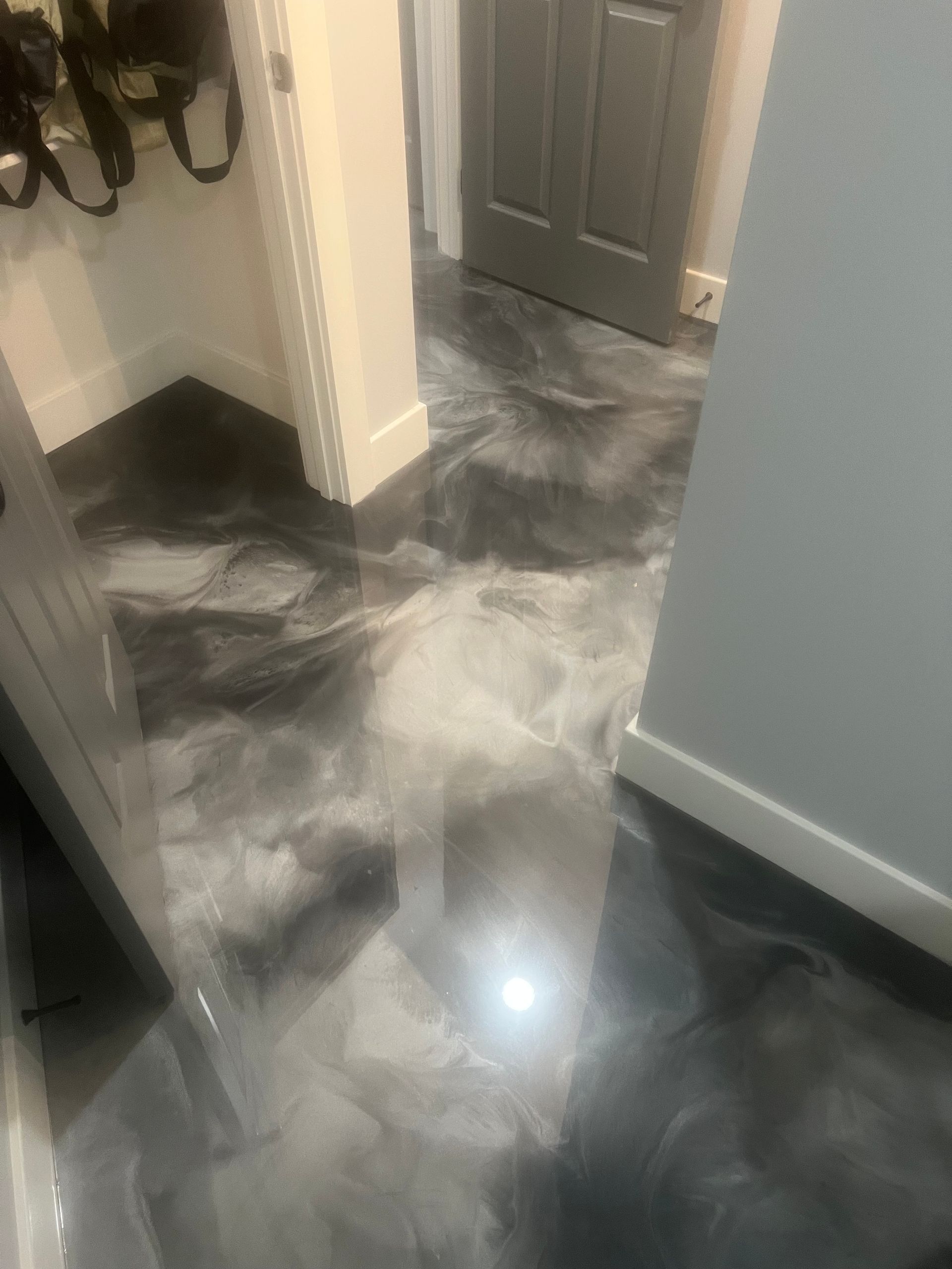 A hallway with a smooth, glossy floor featuring a marbled, swirling pattern of metallic black, gray, and white tones.