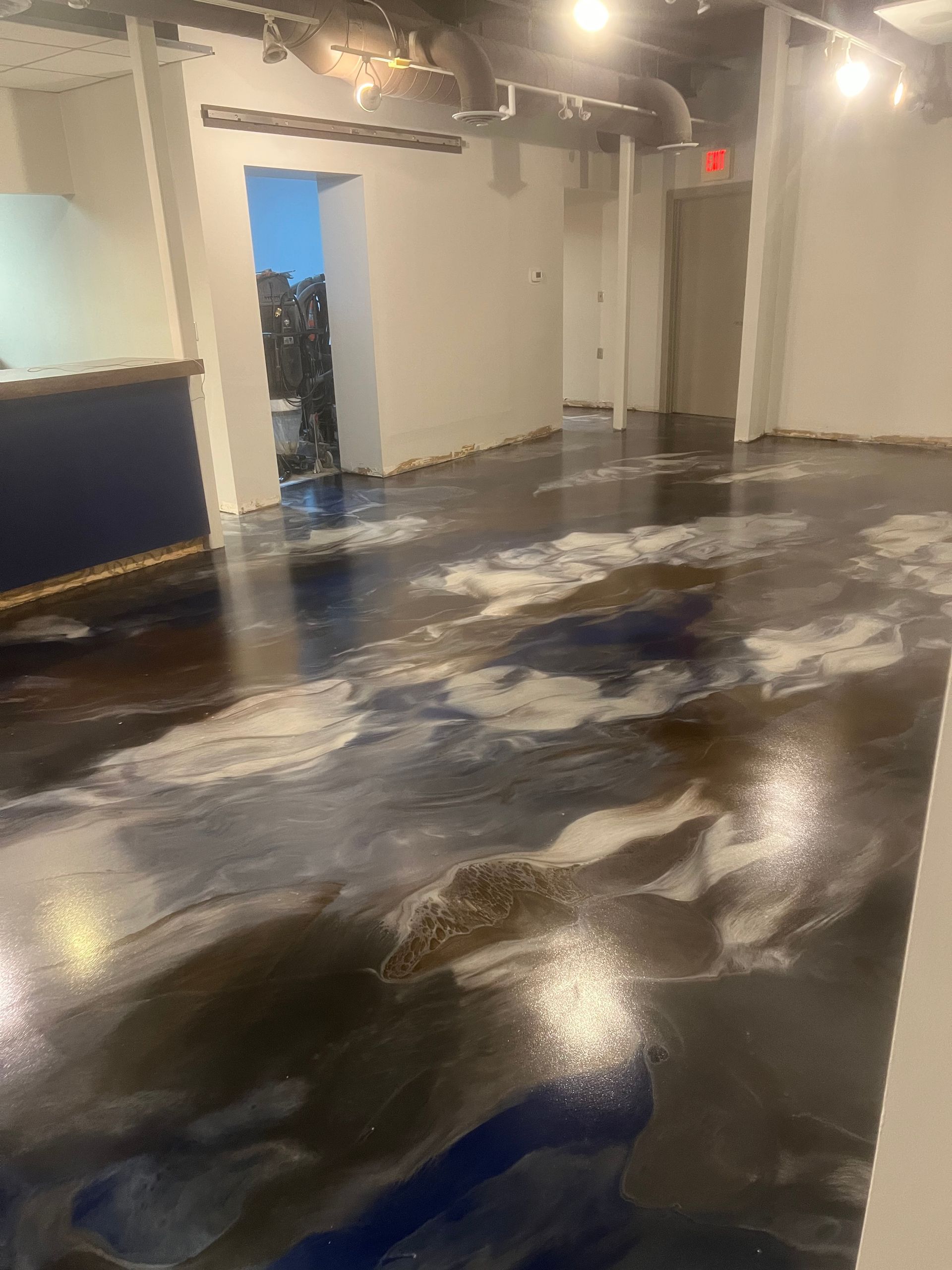 Modern interior room with a dark, marbled blue and white epoxy floor, white walls, and industrial-style ceiling lights.