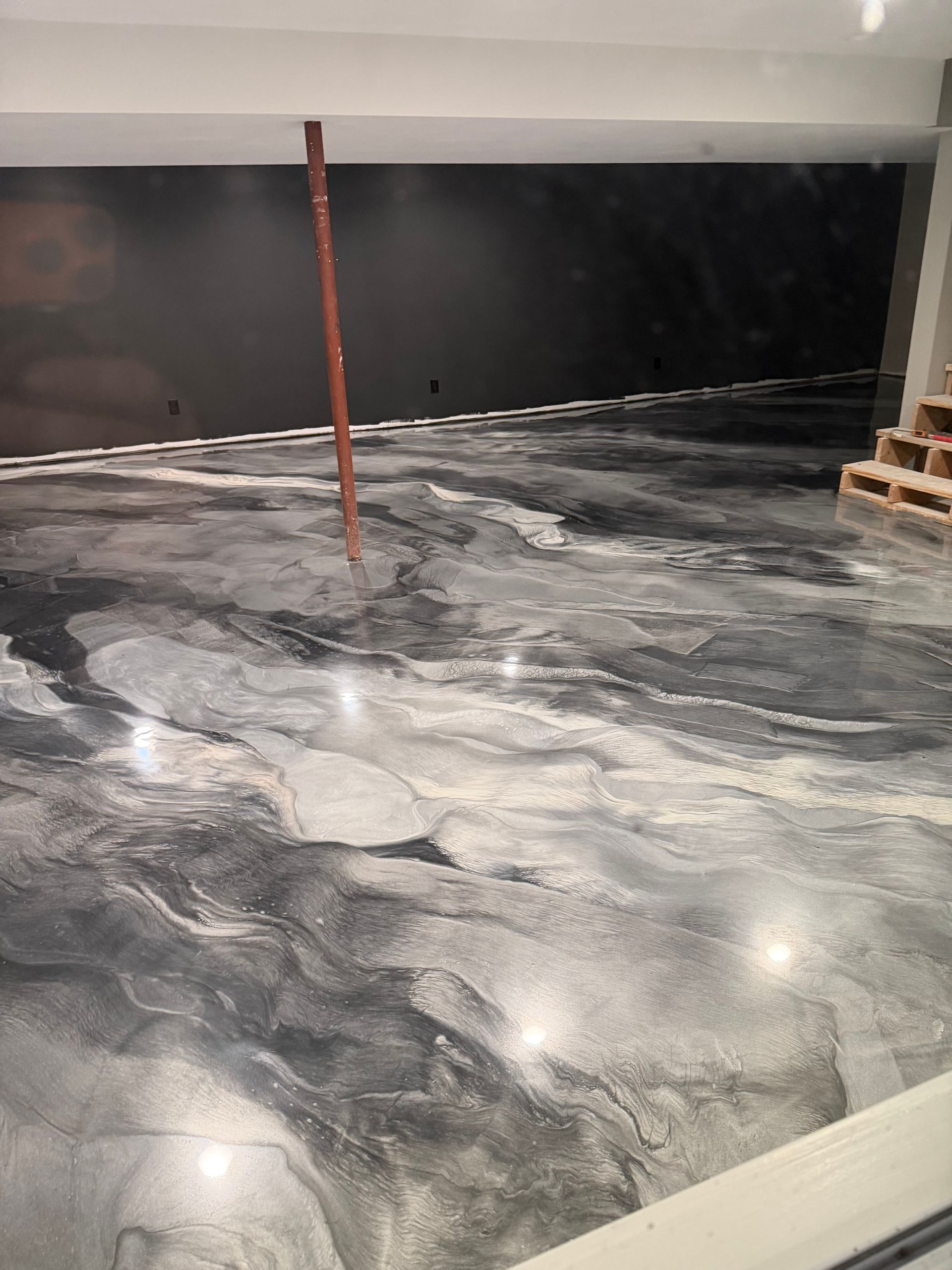 A smooth, glossy gray and black marbled epoxy floor in an unfinished basement room with a central support pole.