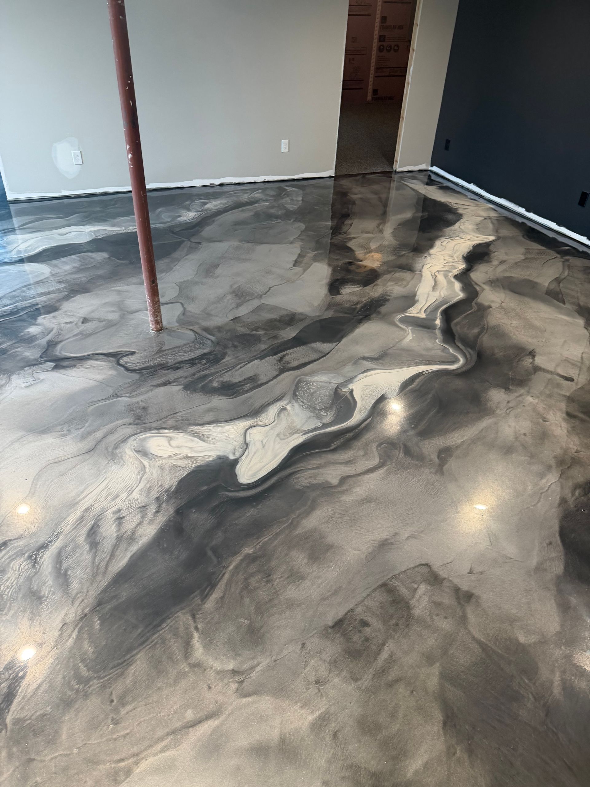 A person wearing a grey glove uses a paint roller to apply grey paint onto a smooth wall surface.