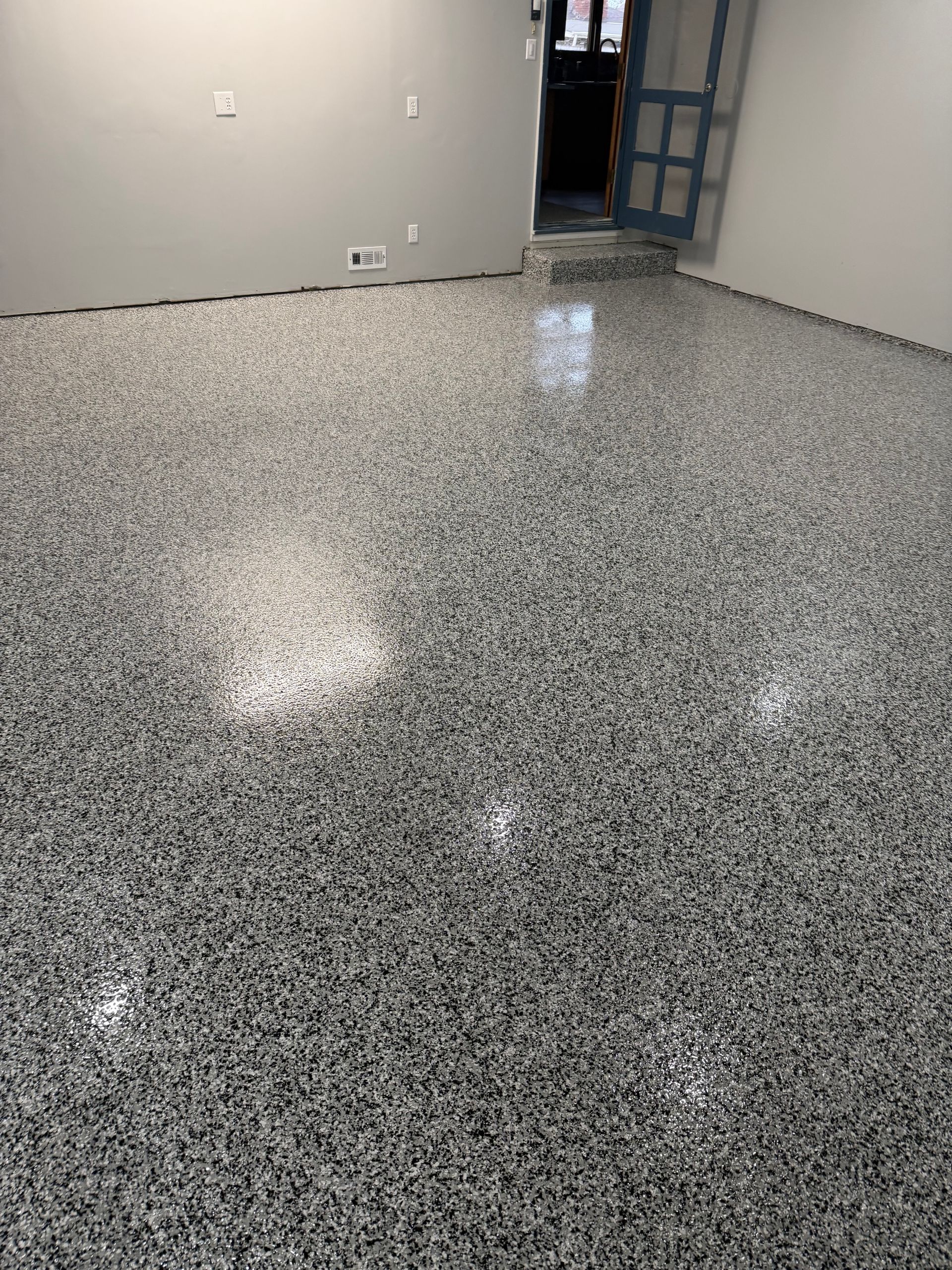 An indoor room with a high-gloss, gray and white speckled epoxy floor and plain light-colored walls.