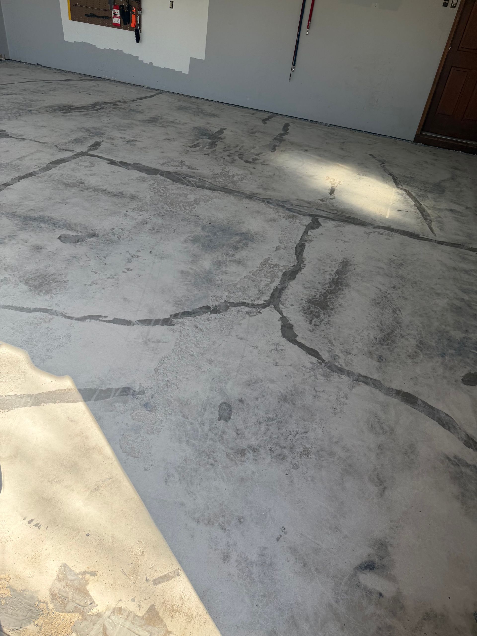 A concrete floor with a network of cracks, viewed from an elevated angle inside a garage.