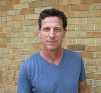 A man in a blue shirt is standing in front of a brick wall