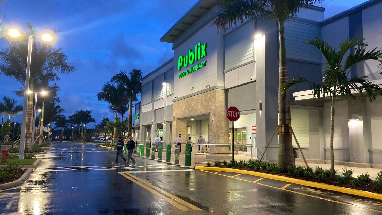 A couple of people are walking down a wet street in front of a publix store.