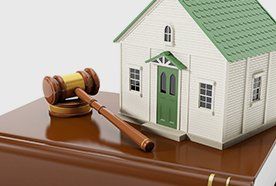A hammer and gavel on a table with a white model house with green roof and door