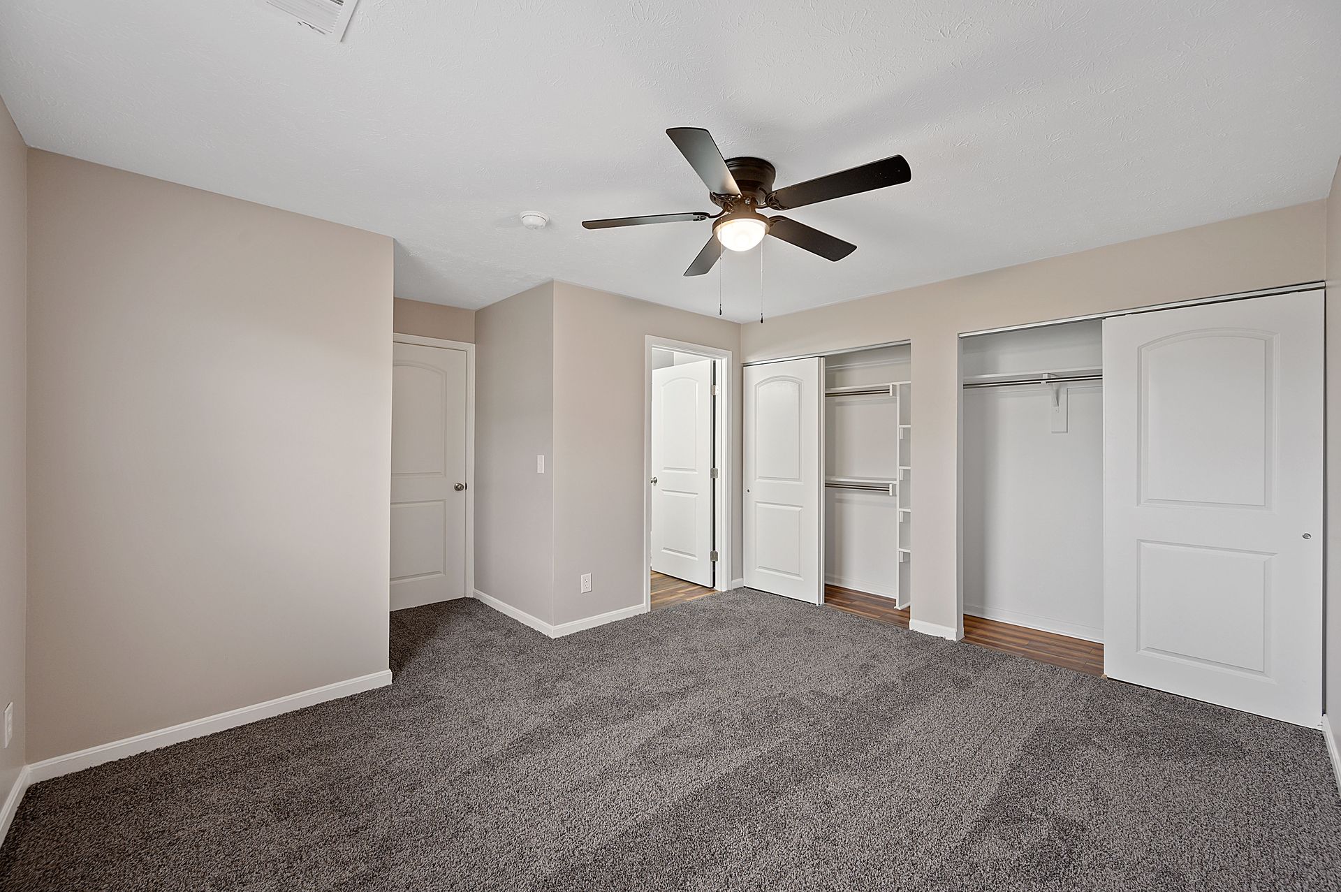 an empty bedroom with a ceiling fan and a lot of closets .