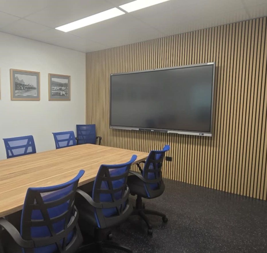 Conference room with a large screen on a wood-paneled wall, a wooden table, and blue-backed chairs.