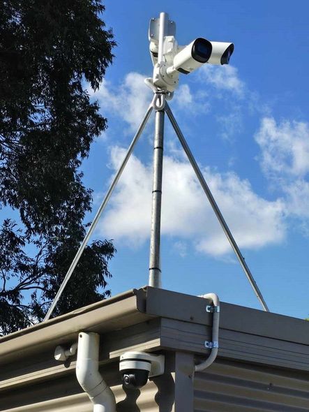 A security camera on top of a building with a tree in the background.