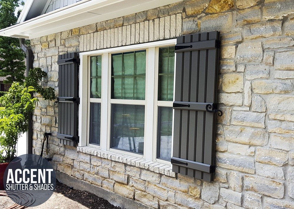A stone house with a window with black shutters on it.