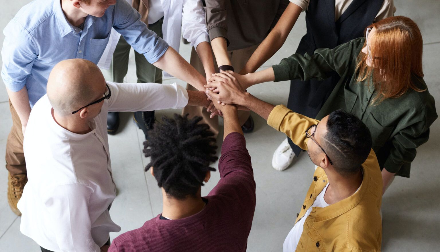 Team of diverse people with hands stacked together in a circle, symbolizing unity.