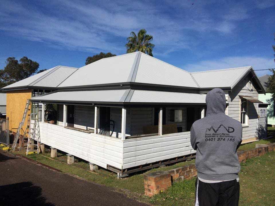 A Man in A Hoodie Is Standing in Front of A White House with New Installed Roof — Mad About Metal Roofing & Guttering PTY LTD in Newcastle, NSW