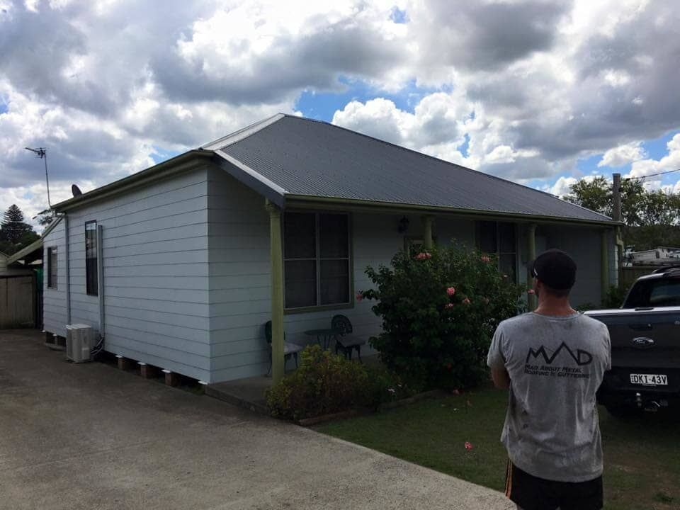 A Man Is Standing in Front of A White House — Mad About Metal Roofing & Guttering PTY LTD in Newcastle, NSW