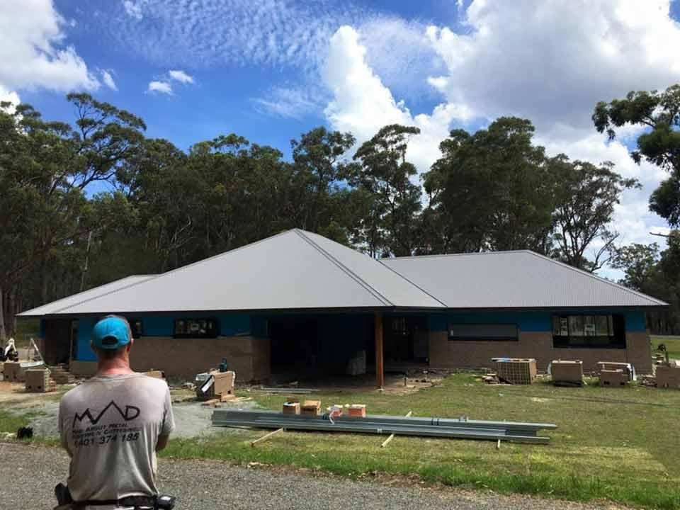 A Man Wearing A Blue Cap Is Standing In Front Of A House Under Construction — Mad About Metal Roofing & Guttering PTY LTD in Newcastle, NSW