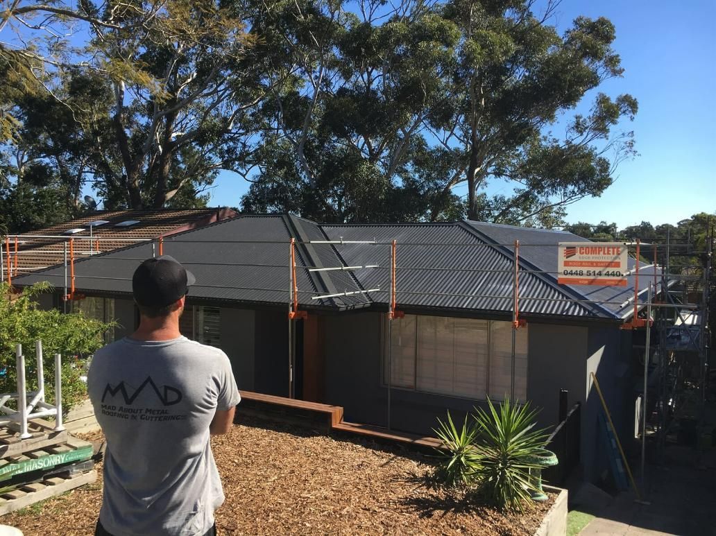 A Man Is Standing in Front of A House Under Construction — Mad About Metal Roofing & Guttering PTY LTD in Newcastle, NSW