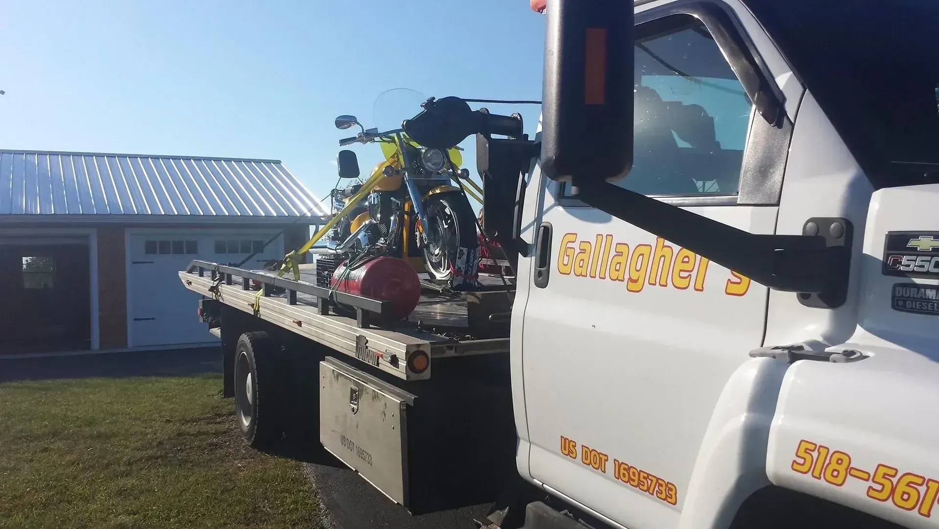 A tow truck with a motorcycle on the back is parked in front of a garage.