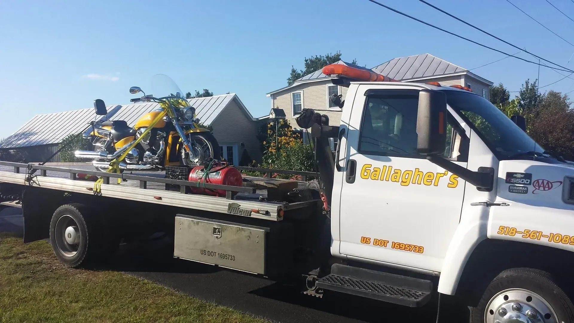 A tow truck with a motorcycle on the back is parked in front of a house.